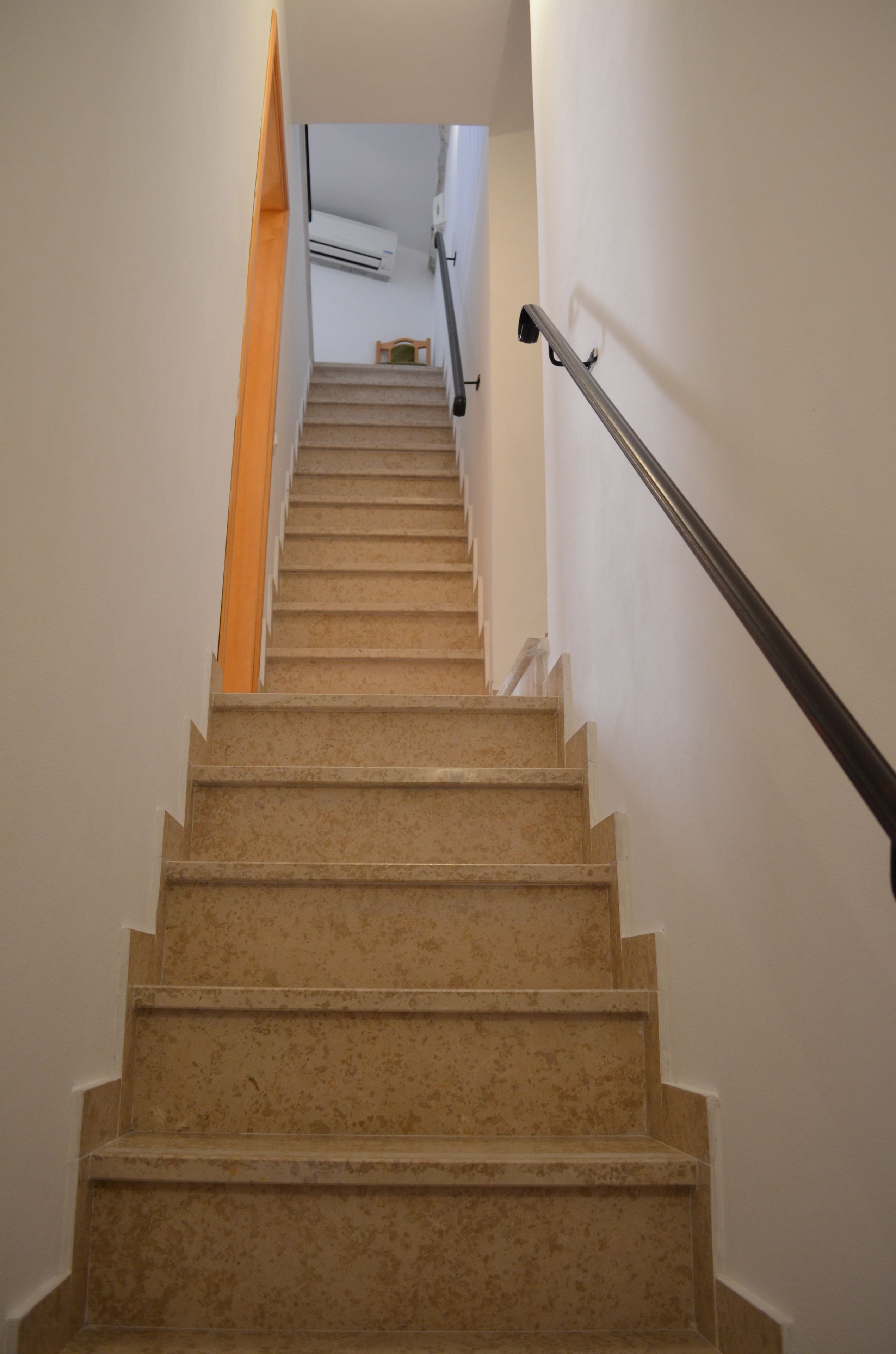Un escalier recouvert de moquette, doté d’une rampe, mène à un palier où se trouve un appareil de climatisation et une petite table.