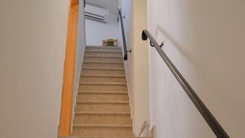 A carpeted staircase with a handrail, leading to a landing with an air conditioning unit and a small table.