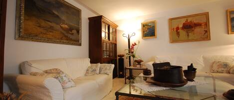 A living room with a white sofa, a glass coffee table, and a large painting on the wall.