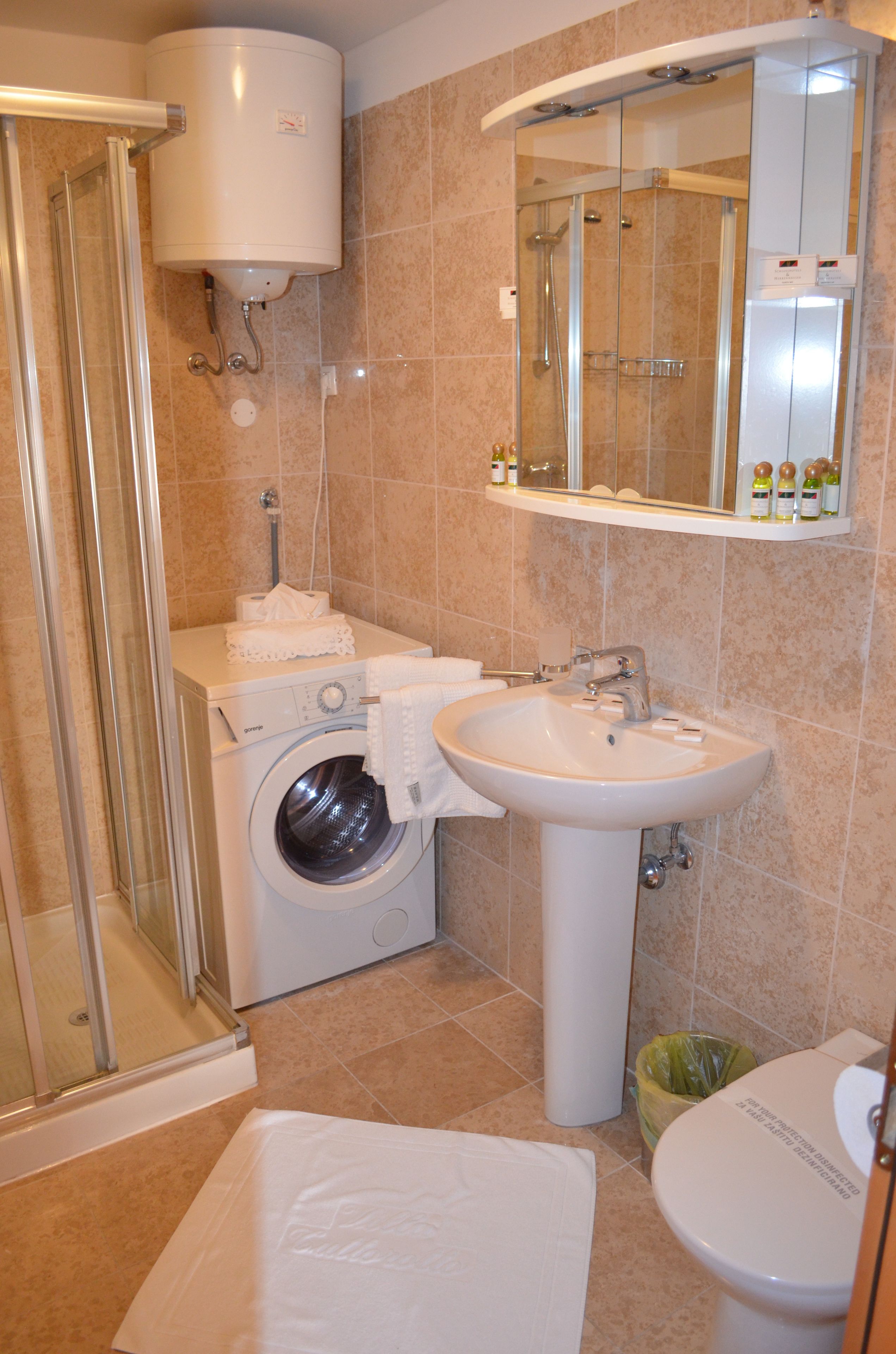 A compact bathroom with a washing machine, a sink, and a toilet.
