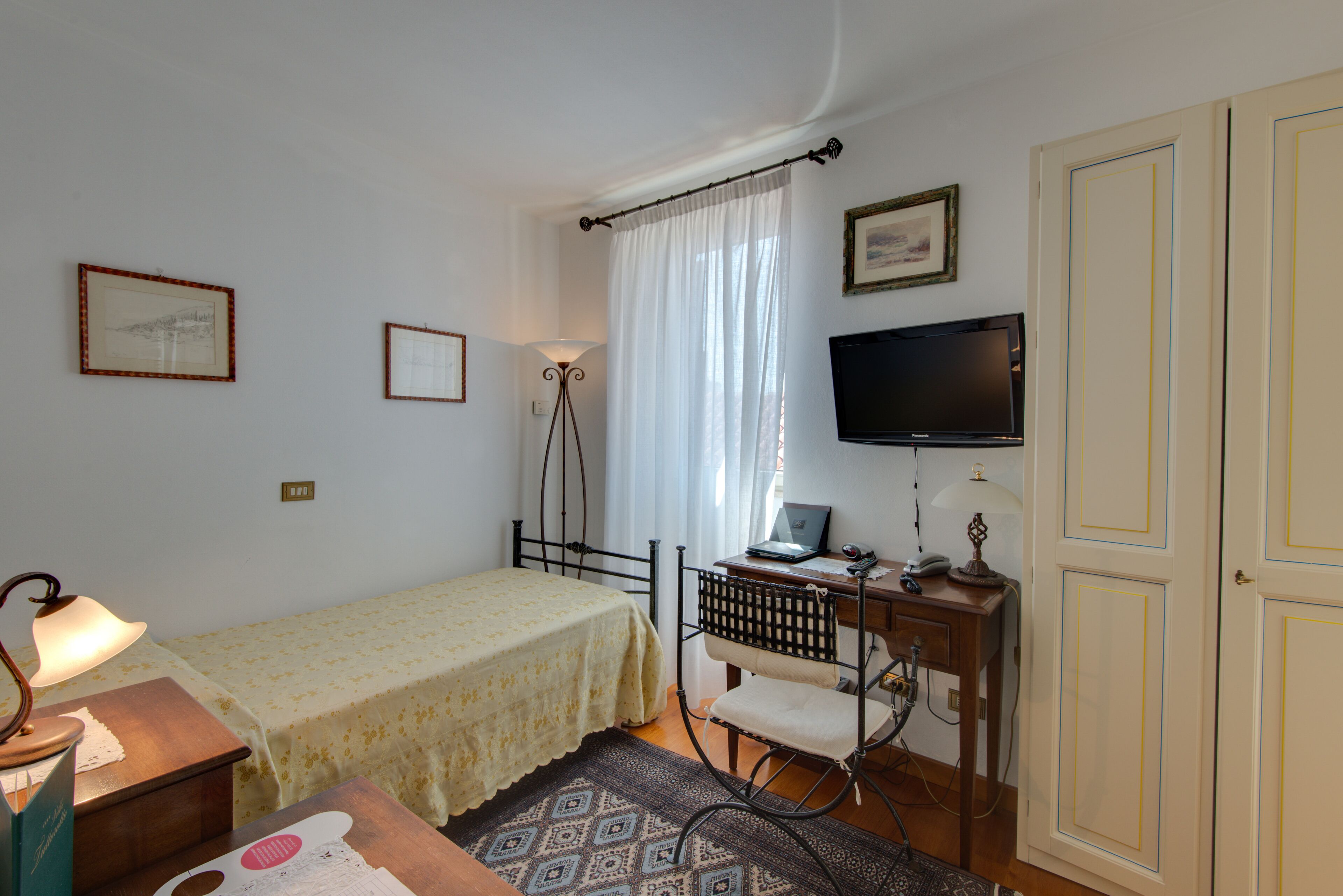 A room with a bed, desk, chair, lamp, television, and wardrobe.