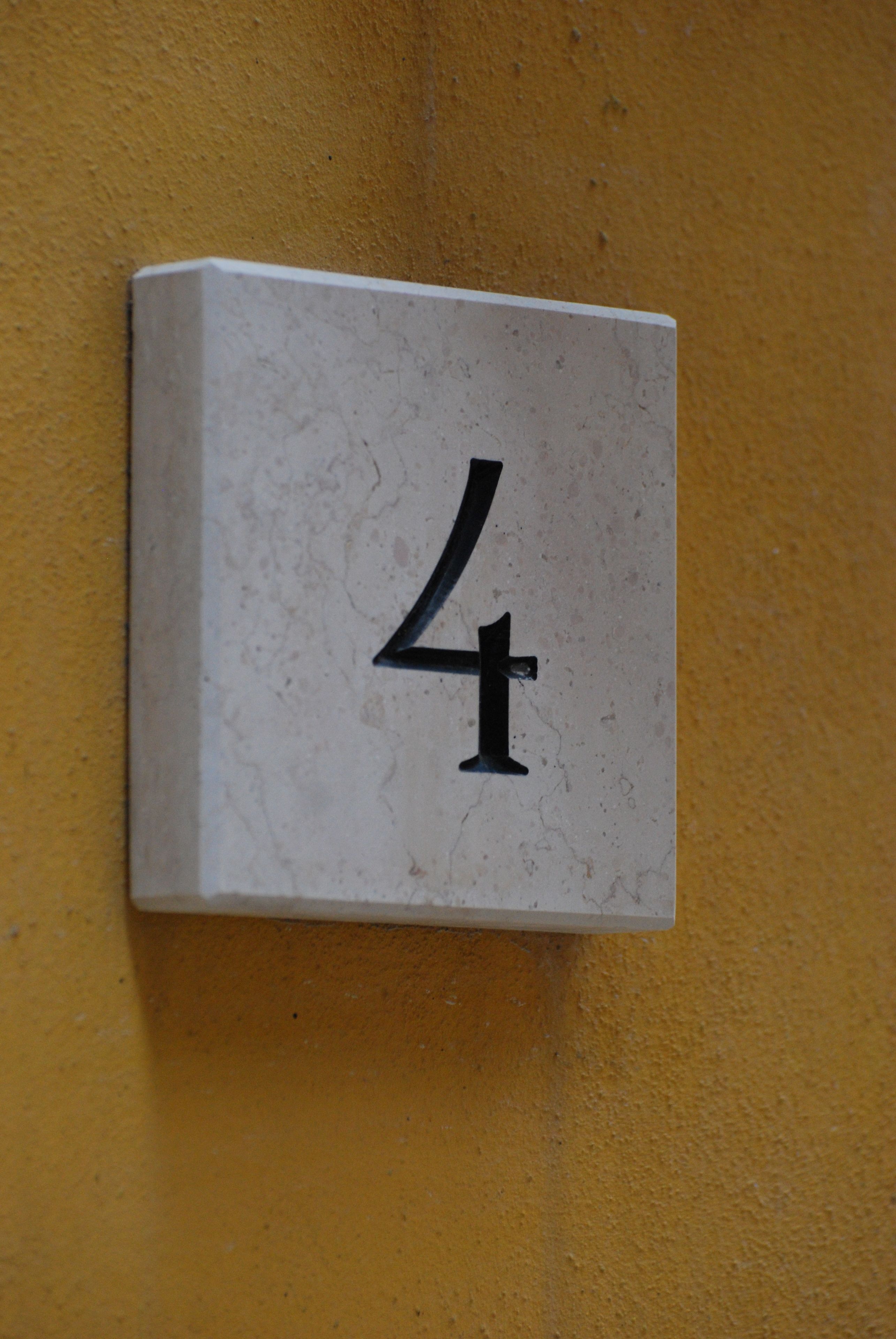 Placa com o número 4, em branco, numa parede amarela.