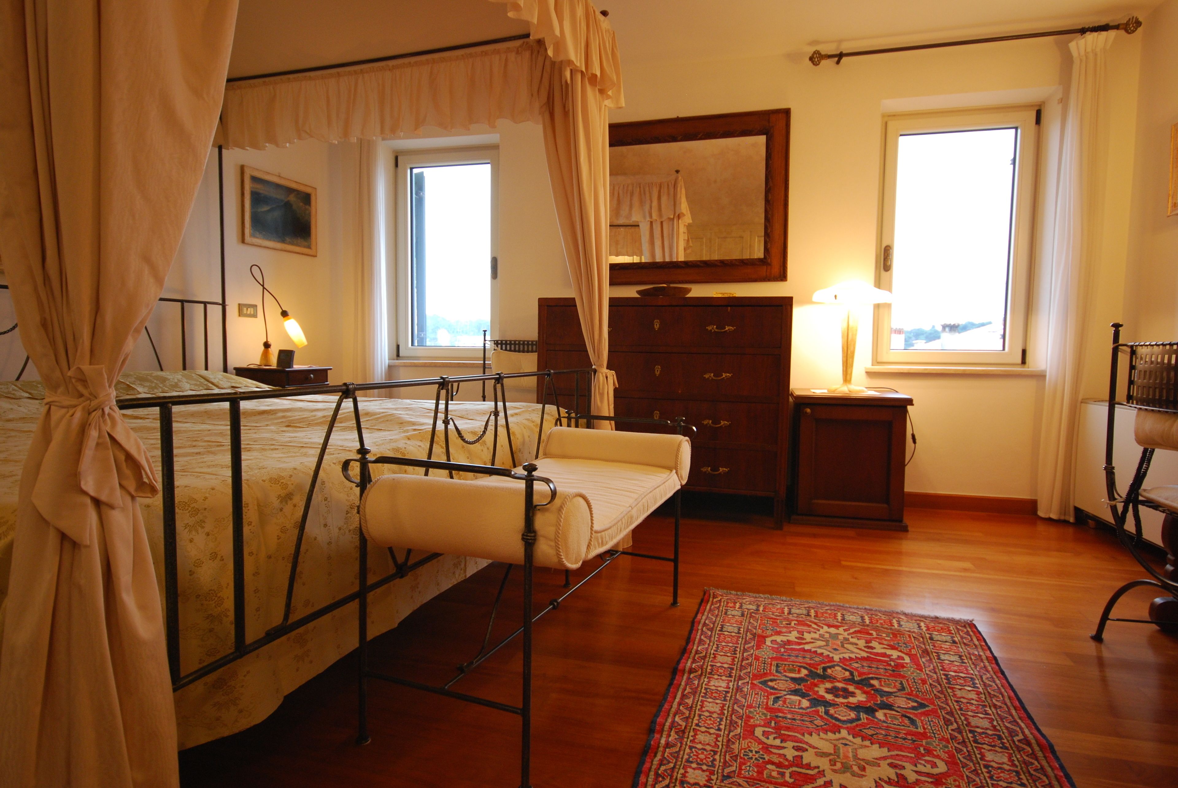 Un dormitorio con cama con dosel, cómoda de madera, espejo y ventana con cortinas.