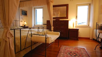 A bedroom with a four-poster bed, a wooden dresser, a mirror, and a window with curtains.