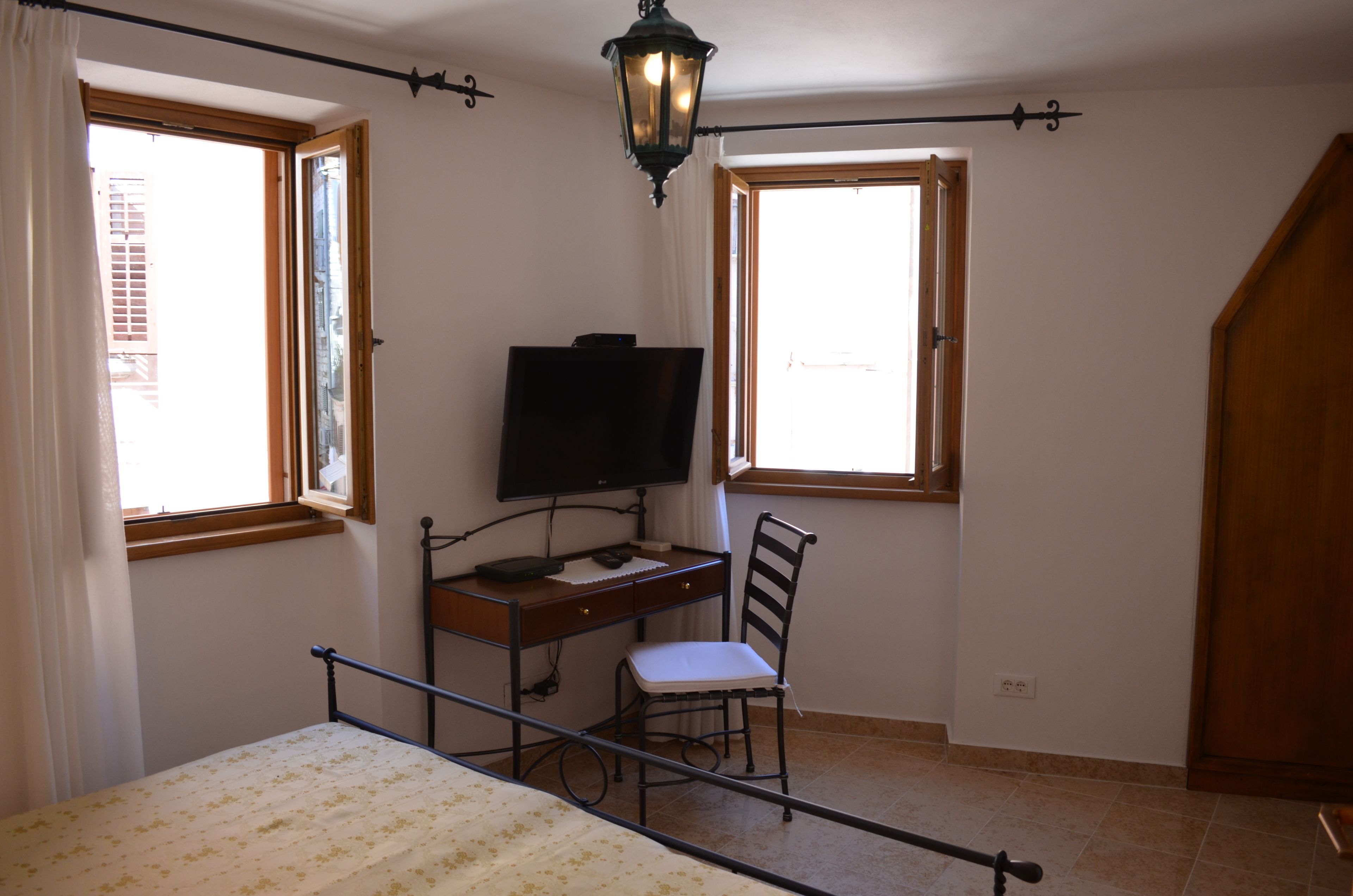A bedroom with a bed, a desk, a chair, a television, and two windows.