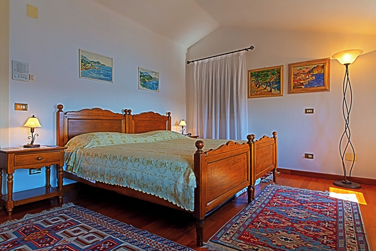 A bedroom with a wooden bed, a nightstand, a lamp, a floor lamp, and a patterned rug.