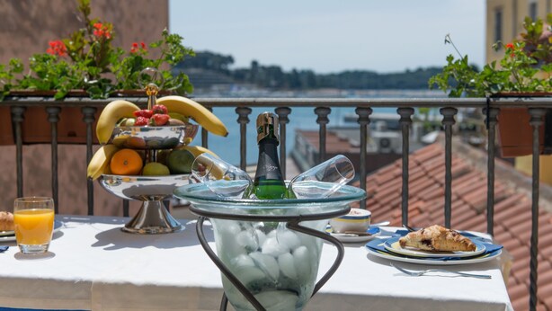 Una mesa con un frutero, una botella y un vaso de jugo de naranja en un balcón con vista a la ciudad.