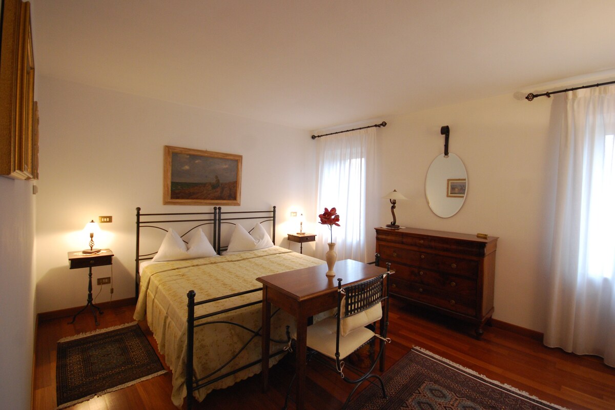 A bedroom with a bed, bedside table, lamp, dresser, and a painting on the wall.