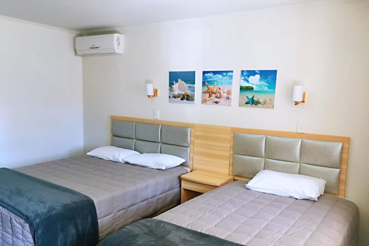 A hotel room with two beds, a wooden headboard, and three wall-mounted pictures depicting beach scenes.