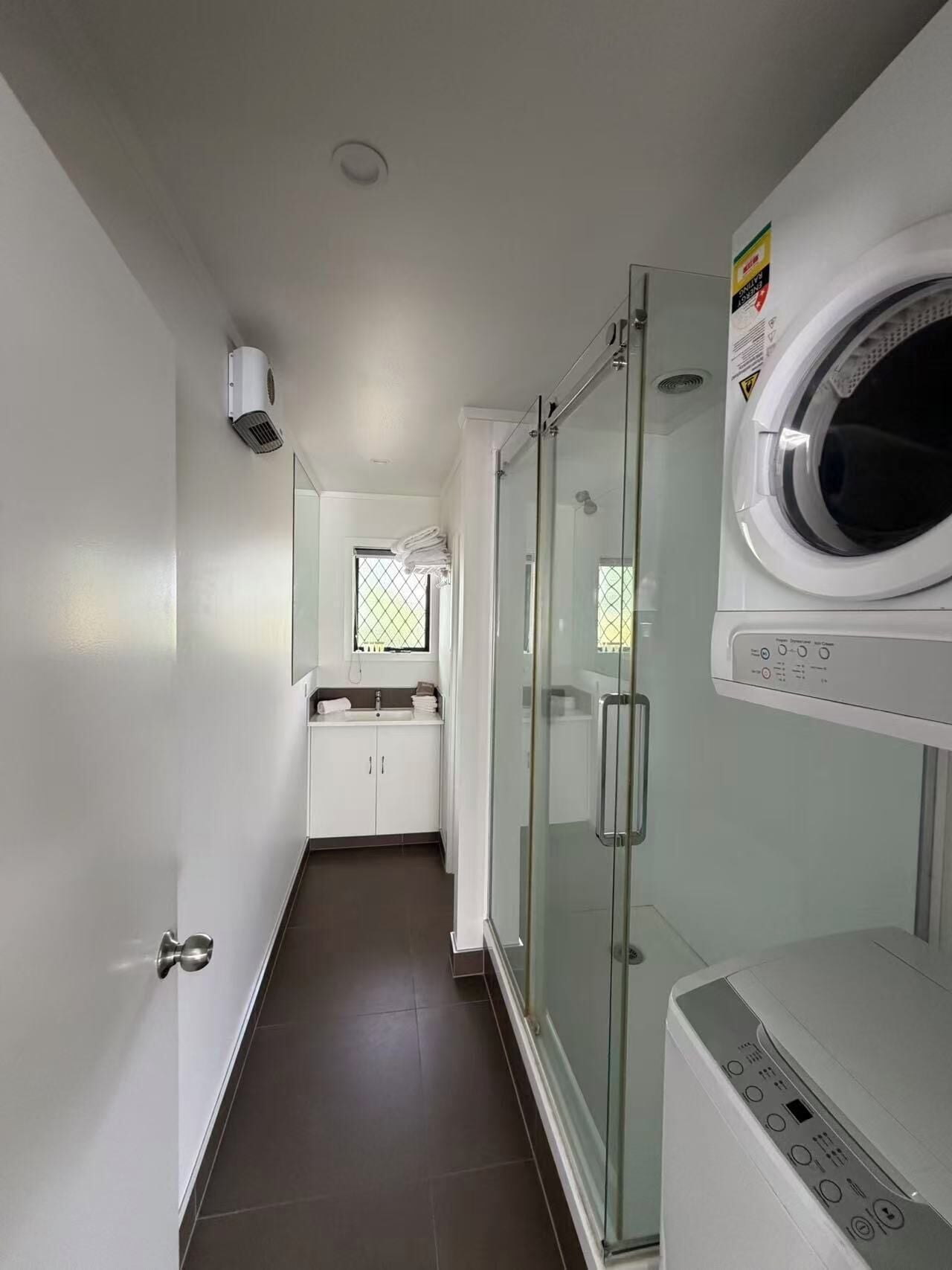 Une buanderie équipée d’un lave-linge, d’un sèche-linge et d’une cabine de douche en verre.