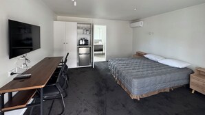 A compact hotel room with a bed, a desk with chairs, a TV, and a kitchenette. - Grosvenor Motor Inn (Hamilton)