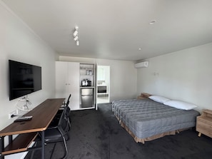 Habitación de hotel compacta con cama, escritorio con sillas, televisor y kitchenette.