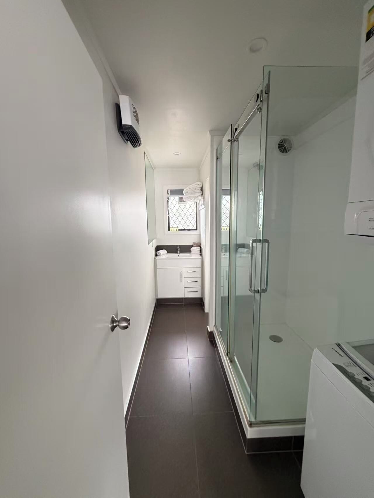 A narrow hallway leading to a bathroom with a glass shower enclosure and a white sink.