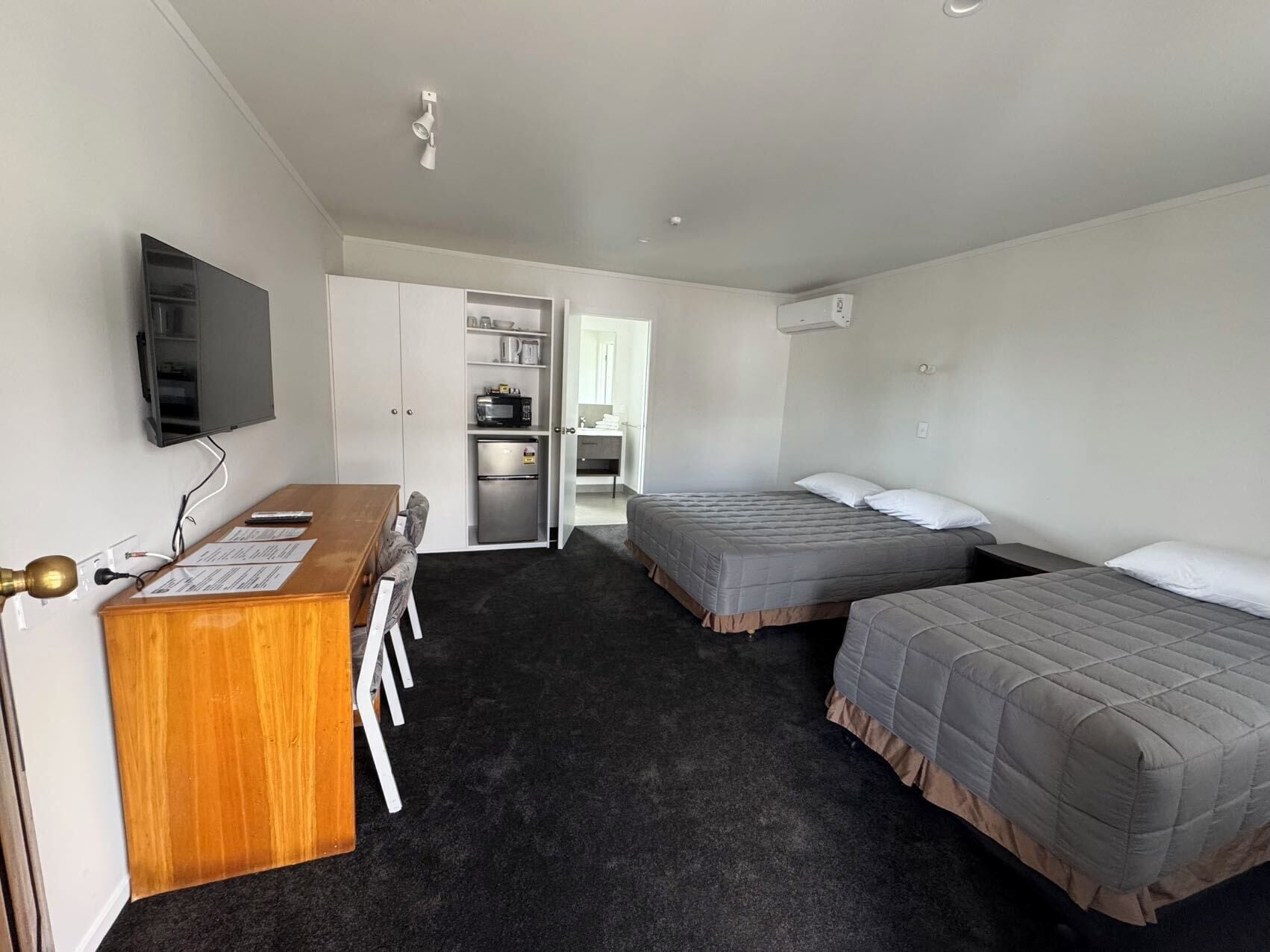 Une chambre d’hôtel équipée d’un bureau, de deux lits, d’une télévision et d ’une kitchenette.