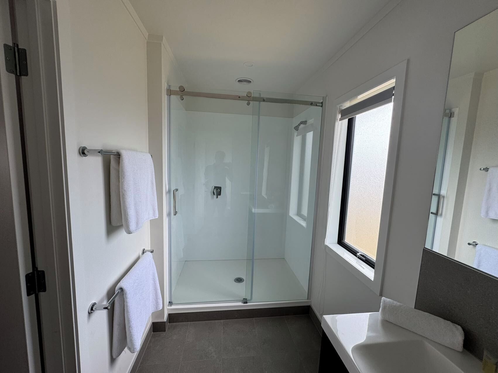 Ein modernes Badezimmer mit Duschkabine aus Glas, einem weißen Waschbecken und einem Fenster für natürliches Licht.