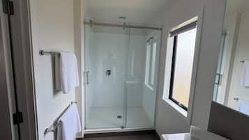 A modern bathroom with a glass shower enclosure, a white sink, and a window providing natural light.