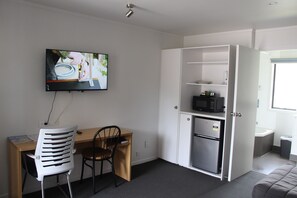 A compact room with a desk, chair, television, microwave, and a small refrigerator.