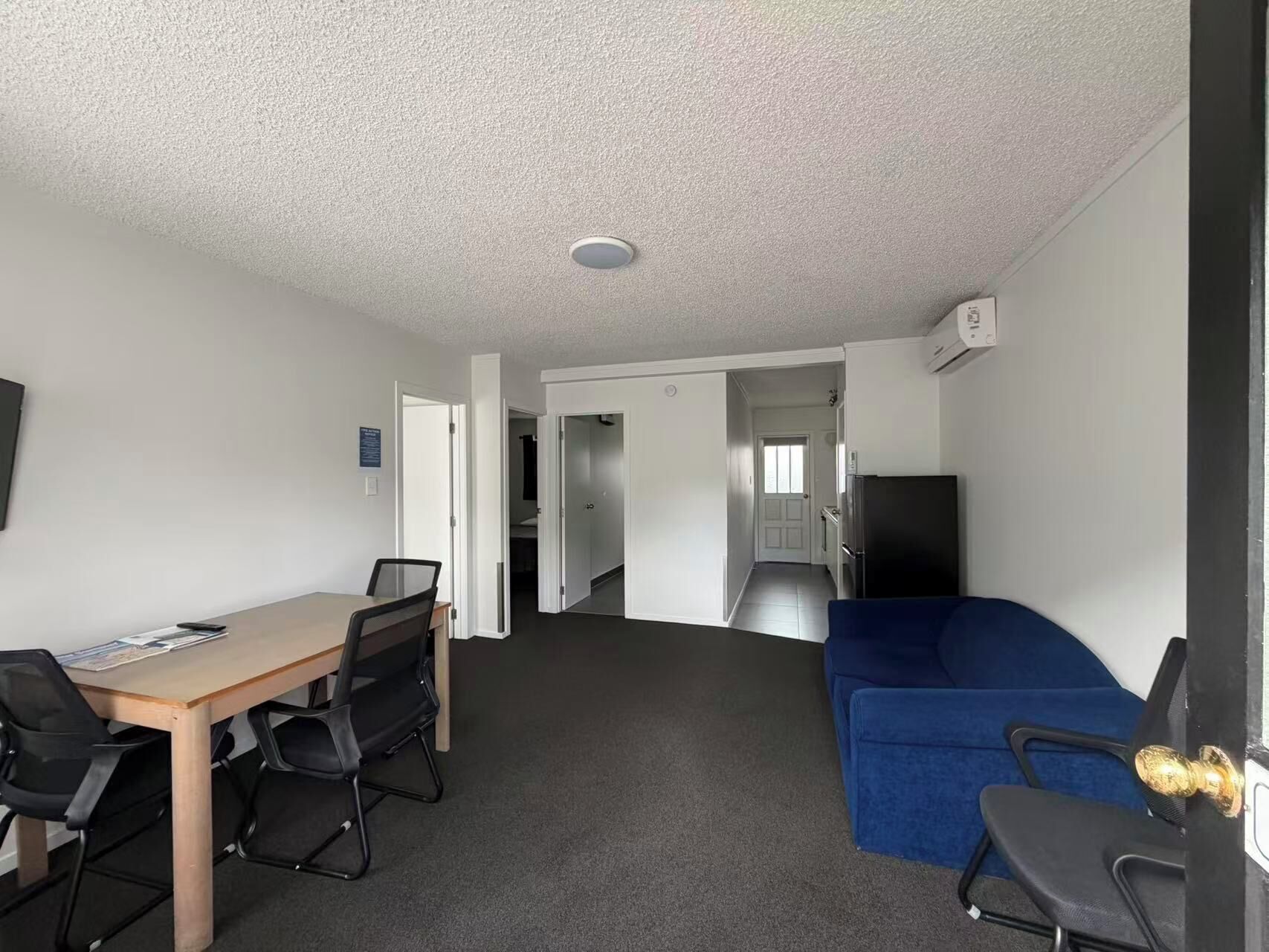 A room with a wooden table, two chairs, a blue sofa, and a kitchenette area.