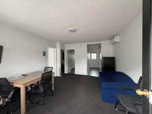 A room with a wooden table, two chairs, a blue sofa, and a kitchenette area. - Grosvenor Motor Inn (Hamilton)