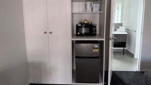 A compact kitchen with a built-in microwave, a small refrigerator, and a shelf with kitchenware. - Grosvenor Motor Inn (Hamilton)