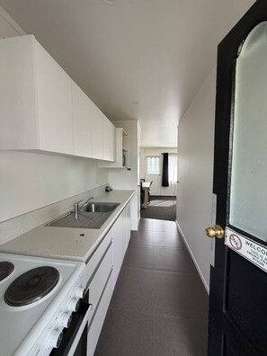 A modern kitchen with white cabinets, a stainless steel sink, and a stove. - Grosvenor Motor Inn (Hamilton)