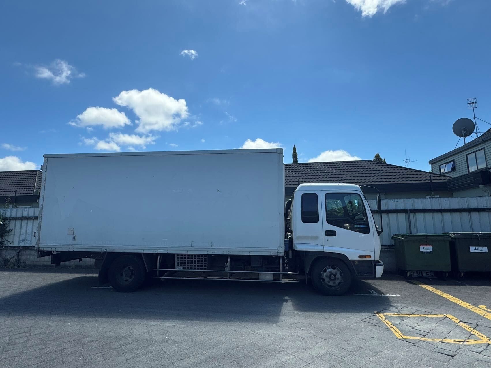 Een witte bestelwagen staat geparkeerd op een parkeerplaats, met gebouwen op de achtergrond.