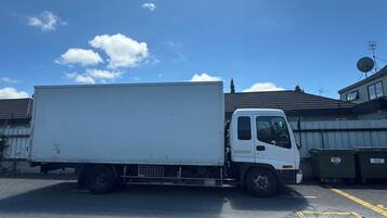 Een witte bestelwagen staat geparkeerd op een parkeerplaats, met gebouwen op de achtergrond.