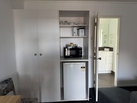 Una kitchenette compacta con microondas, un refrigerador pequeño y una alacena con utensilios de cocina.