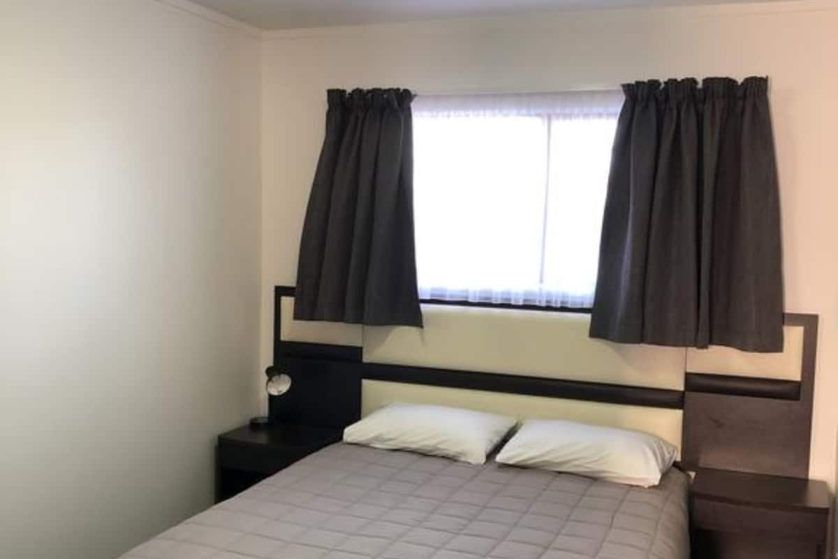A single bed with a headboard, two bedside tables, a nightstand, and a window with curtains.
