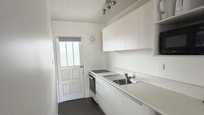 A compact kitchen with white cabinets, a stainless steel sink, a microwave, and a trash bin. - Grosvenor Motor Inn (Hamilton)