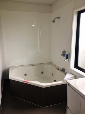 A modern bathroom with a large freestanding bathtub, a showerhead, and a window. - Grosvenor Motor Inn (Hamilton)