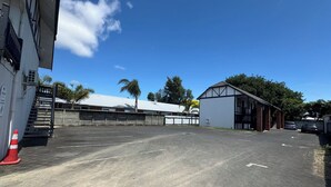 A parking lot with a building on the left and a white structure with a sloped roof on the right. - Grosvenor Motor Inn (Hamilton)