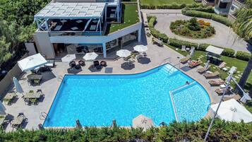 A swimming pool with lounge chairs and umbrellas, surrounded by a landscaped garden and a modern building with a glass facade.