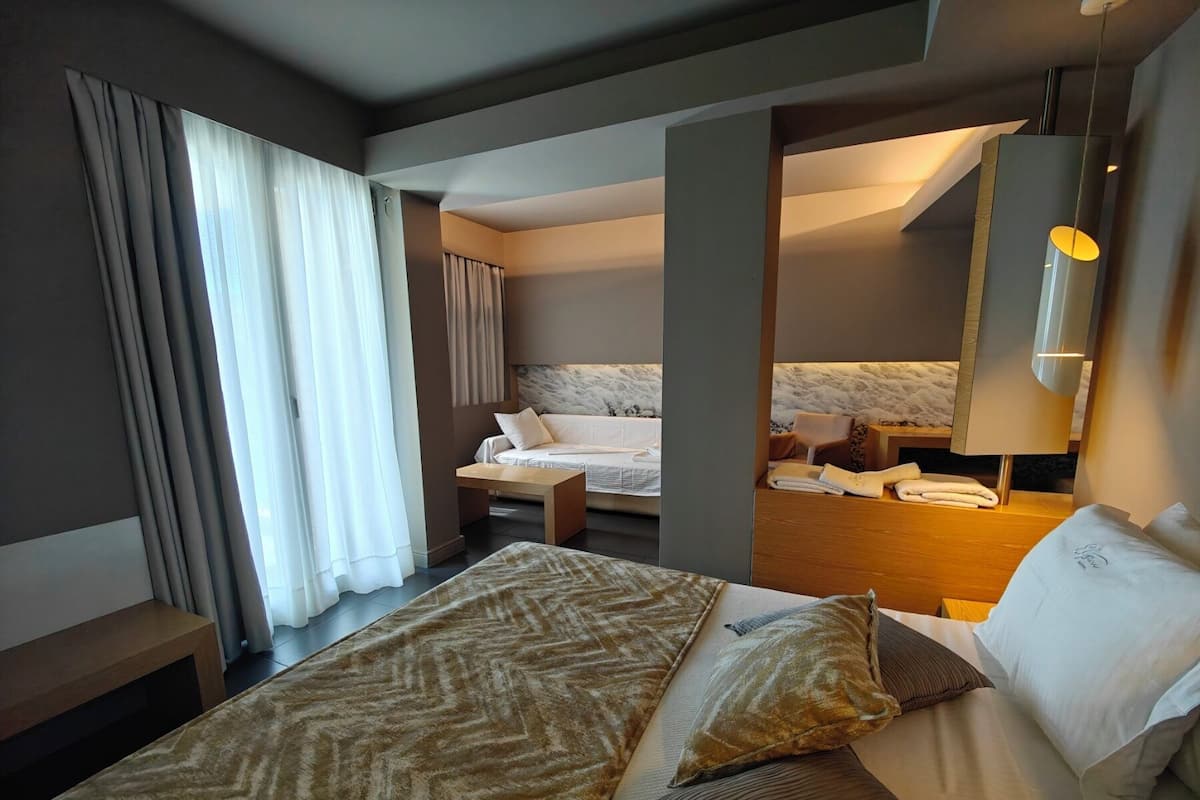 A hotel room with a bed, a sitting area, a bathroom, and a large window with curtains.