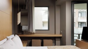 Habitación de hotel con cama, escritorio, televisión y ventana con vistas a edificios.