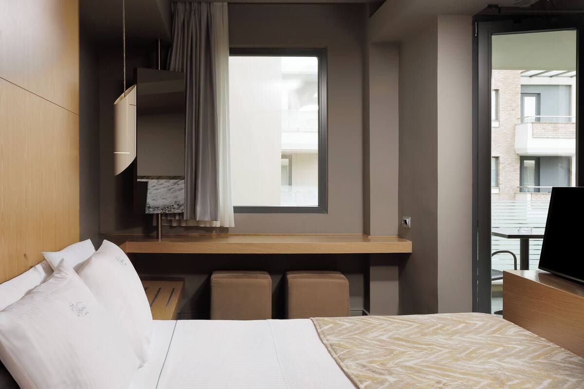 A hotel room with a bed, a desk, a TV, and a window with a view of buildings.