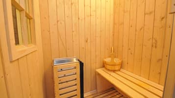 Ein Saunaraum aus Holz mit einer Bank, einem Holz-Eimer und einem Metallbehälter.