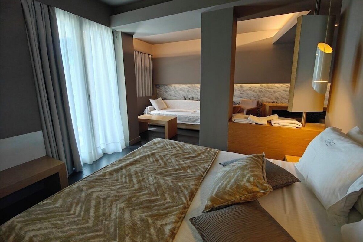 A hotel room with a large bed, a desk, a chair, a sofa, and a mirror.