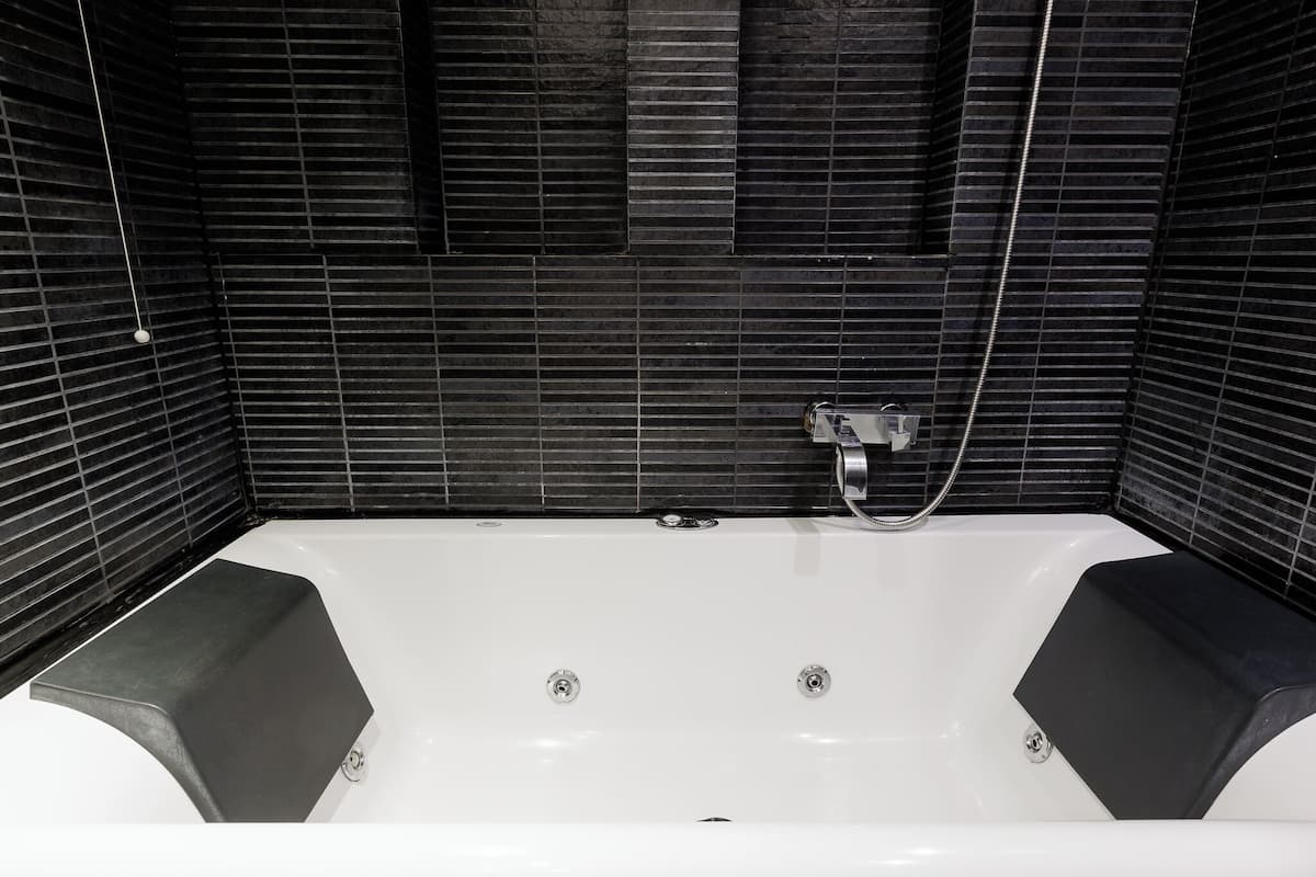 A modern bathroom with a white bathtub, black tiled walls, and a shower area.