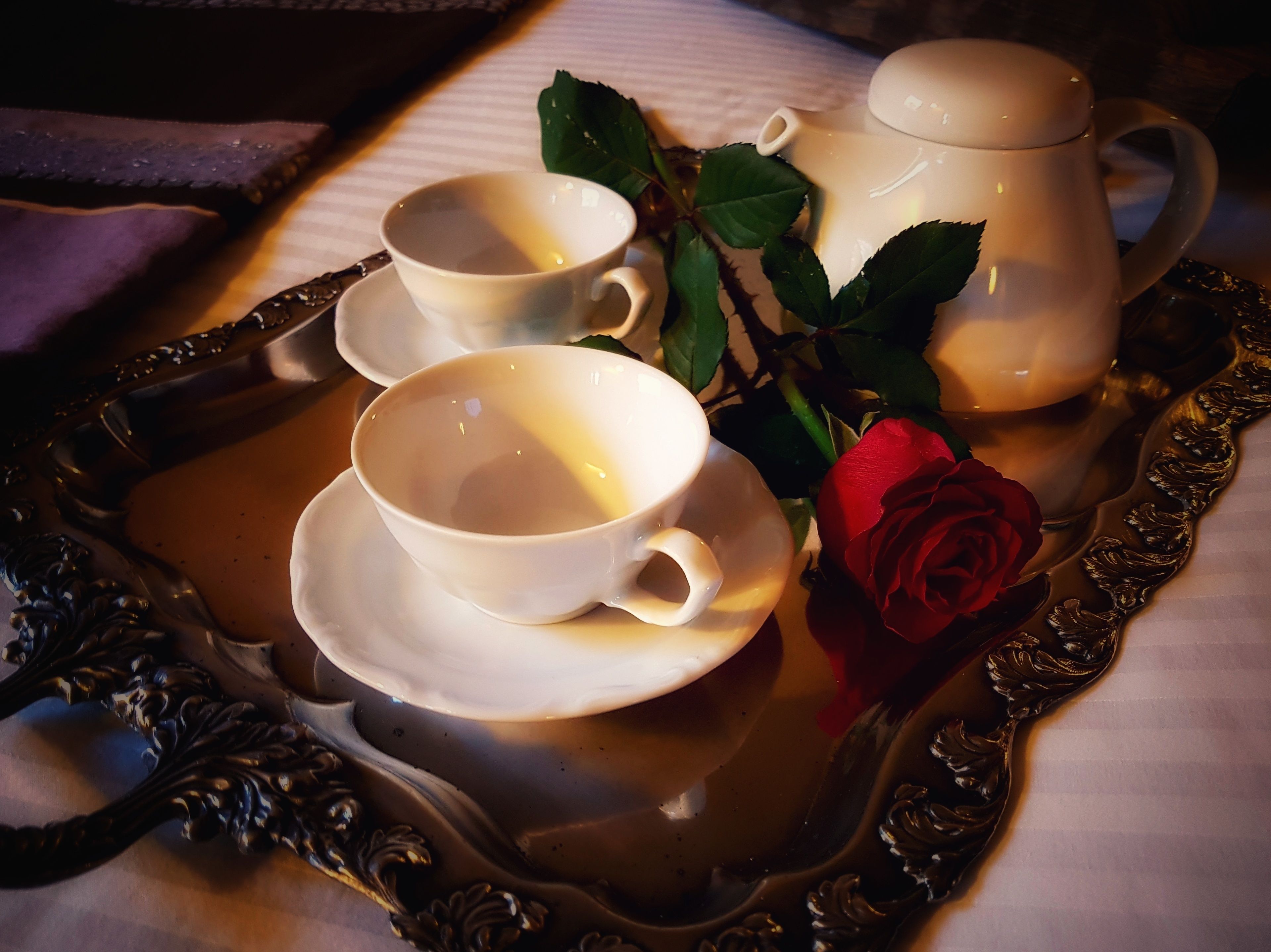 Una bandeja con una tetera, dos tazas y una rosa.