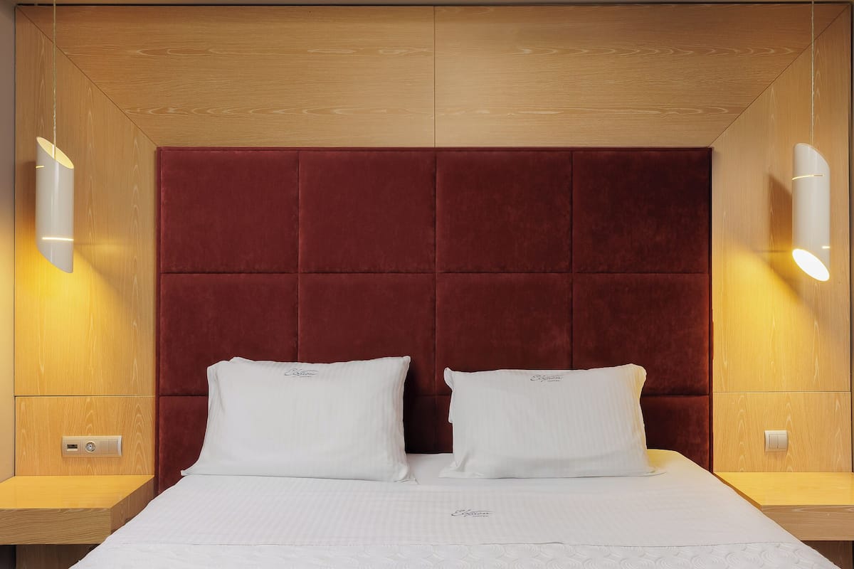 A hotel room with a large bed, two bedside tables, a wooden headboard, and wall-mounted lighting.