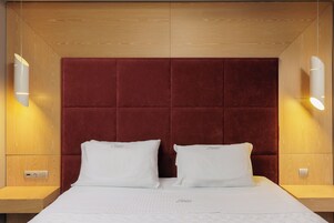 Una habitación de hotel con una cama grande, dos mesitas de noche, un cabecero de madera e iluminación empotrada en la pared.