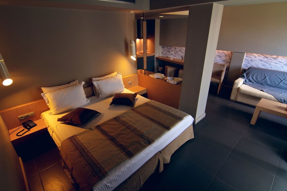 A modern hotel room with a large bed, bedside tables, a desk, a chair, and a bathroom area.