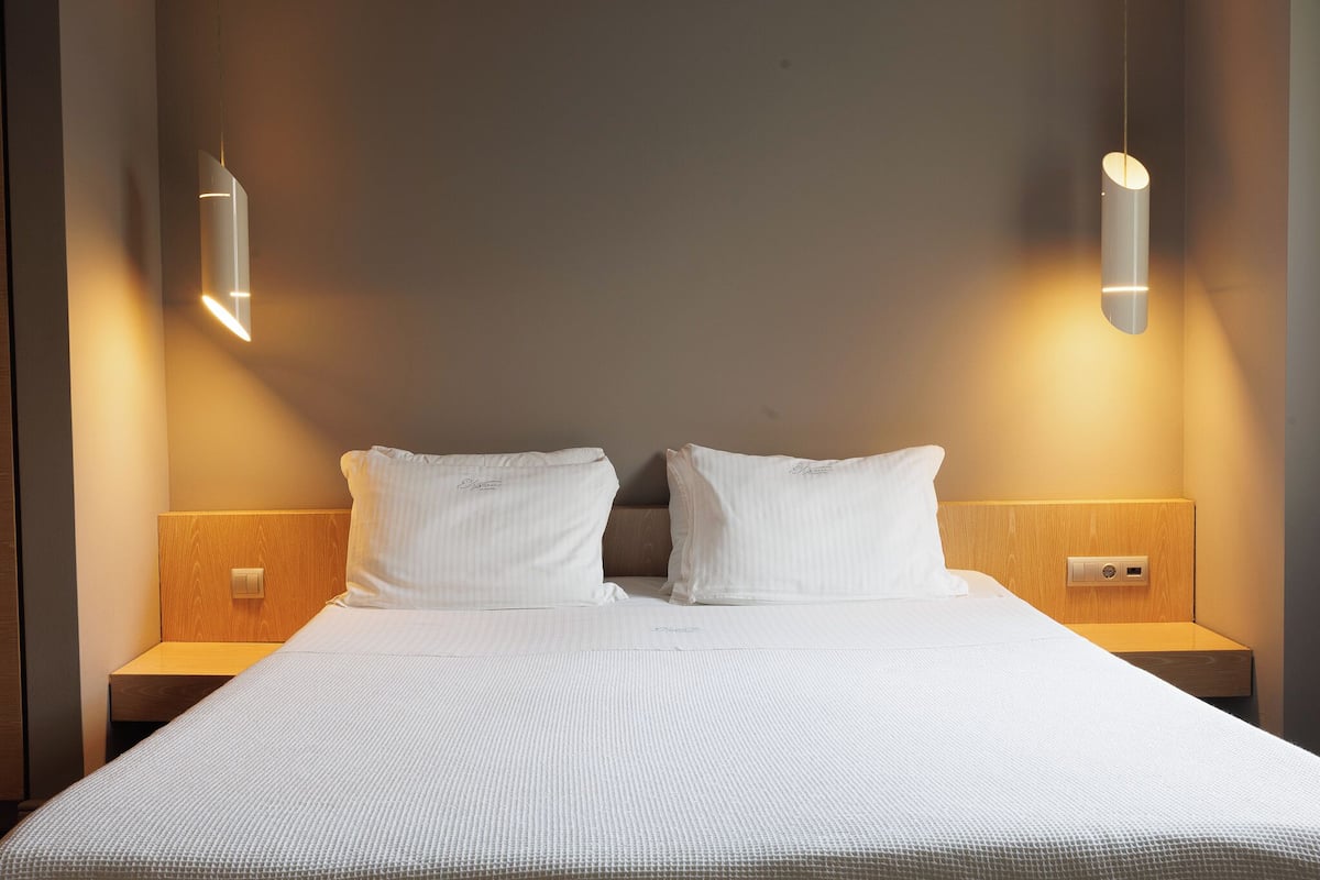 A hotel room with a large bed, two bedside tables, and two wall-mounted lights.