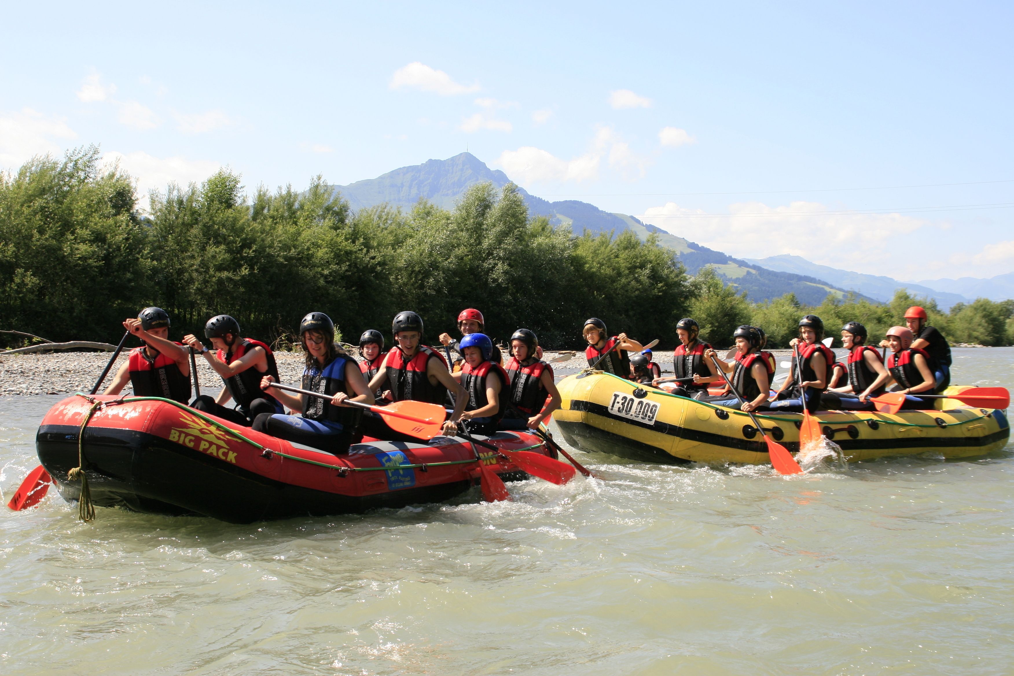 Deux radeaux gonflables sur une rivière, avec des personnes qui les font avancer à l'aide de pagaies.