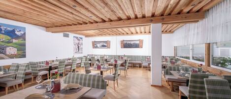 Ein Restaurant mit Holzbalken, karierten Tischdecken und Wandgemälden einer Berglandschaft.