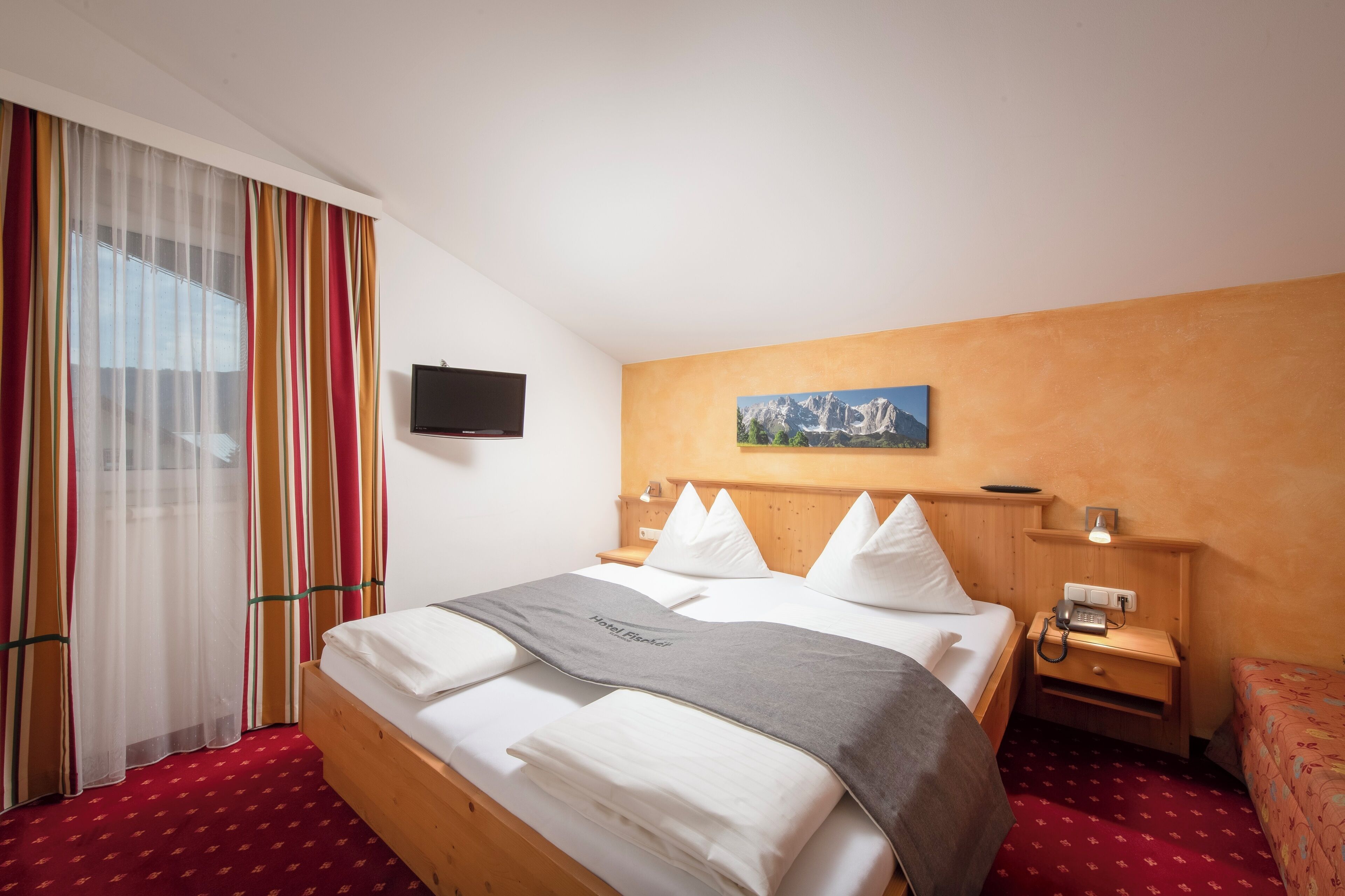 A hotel room with a bed, a TV, a painting, and a wooden headboard.