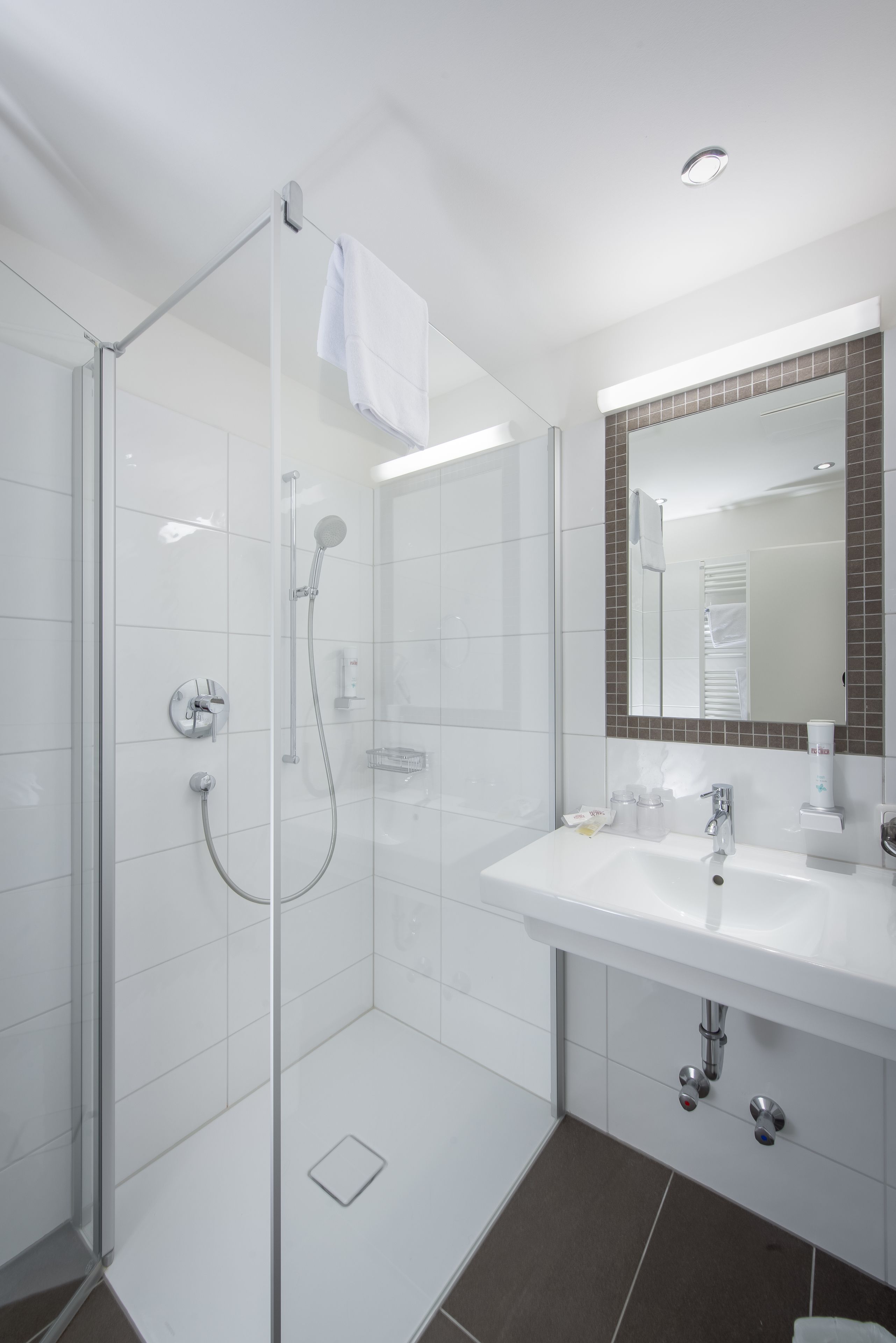 A modern bathroom with a glass-enclosed shower, a white sink, and a mirror with a brown-tiled frame.