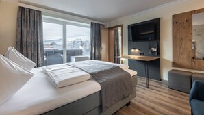 Et moderne hotelværelse med en stor seng, et skrivebord, et fladskærms-tv og udsigt over bybilledet.