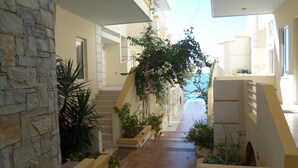 Un couloir avec un mur en pierre d’un côté, un escalier avec une rampe, et une vue sur la mer par une fenêtre.